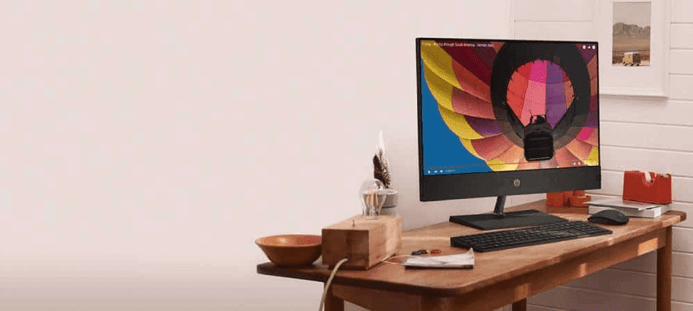 Escritorio minimalista con una computadora todo en uno HP encendida, mostrando una imagen colorida de un globo aerostático en la pantalla